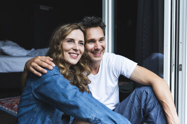 Happy couple in nightwear at home sitting at French window - UUF14347