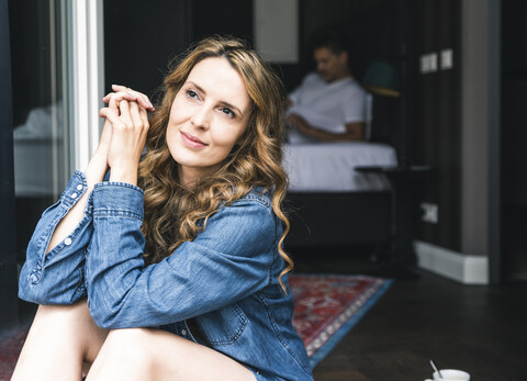 Smiling woman sitting at French window with man in background stock photo