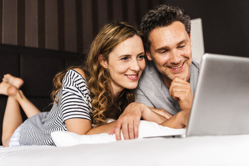 Glückliches Paar, das zu Hause auf dem Bett liegt und auf den Laptop schaut - UUF14372