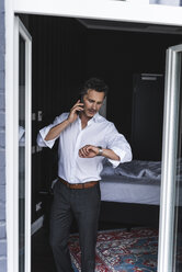 Businessman on cell phone in bedroom at home checking the time - UUF14390