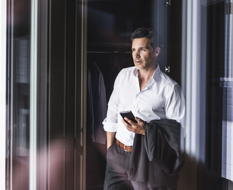 Geschäftsmann mit Mobiltelefon an der Garderobe zu Hause, lizenzfreies Stockfoto