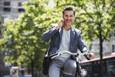 Lächelnder Mann mit Handy auf dem Fahrrad in der Stadt - UUF14412