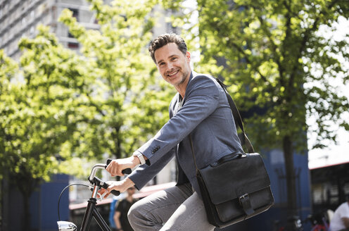 Lächelnder Mann auf dem Fahrrad in der Stadt - UUF14414