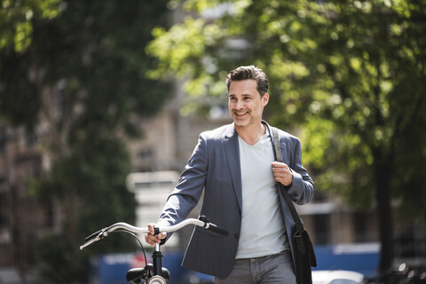 Smiling man pushing bike in the city stock photo