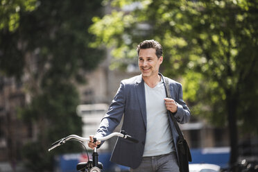 Lächelnder Mann beim Schieben eines Fahrrads in der Stadt - UUF14415