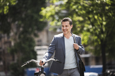 Smiling man pushing bike in the city - UUF14415