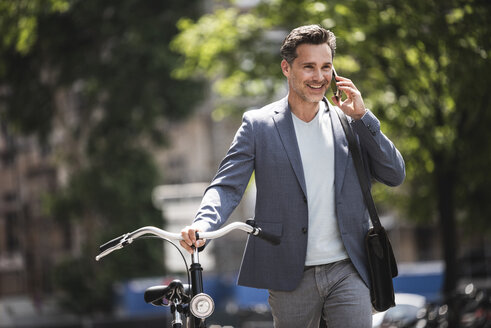 Smiling man on cell phone pushing bike in the city - UUF14417