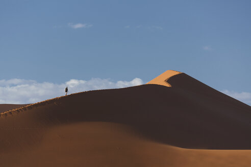 Silhouetted man climbing giant sand dune, Sossusvlei National Park, Namibia - CUF38954