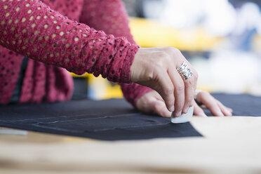 Hände einer reifen Näherin, die mit Kreide Umrisse auf Textilien auf dem Arbeitstisch zeichnet - CUF38977