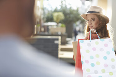 Woman holding shopping bags, looking over shoulder at man - CUF39014