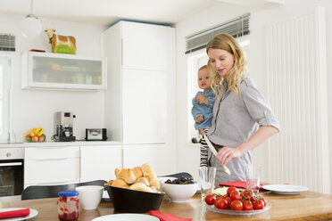 Mutter deckt den Küchentisch und hält ihre kleine Tochter - CUF39034