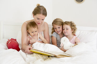Mutter liest drei Töchtern im Bett ein Buch vor - CUF39045