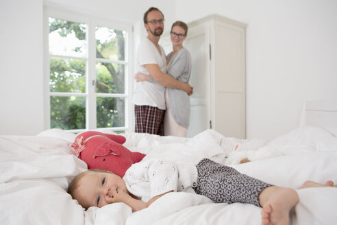 Kleines Mädchen auf dem Bett liegend, Eltern im Hintergrund - CUF39051