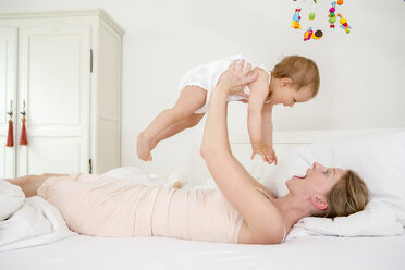 Mother lifting baby daughter on bed - CUF39054