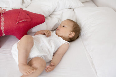 Baby-Mädchen liegt auf dem Bett und betrachtet ein Stofftier - CUF39065