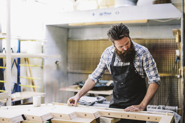 Cropped shot of mid adult craftsman measuring wood in organ workshop - CUF39091