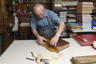 Älterer Mann beim Reparieren eines antiken Buchrückens in einer traditionellen Buchbinderei - CUF39137