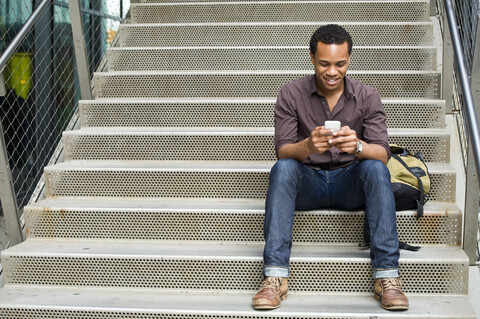 Junger Mann schreibt auf einer Treppe in der Stadt eine SMS mit seinem Smartphone, lizenzfreies Stockfoto