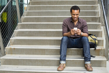 Young man texting on smartphone on city stairway - ISF16490