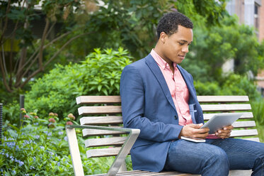 Junger Geschäftsmann sitzt auf einer Parkbank und schaut auf ein digitales Tablet - ISF16492
