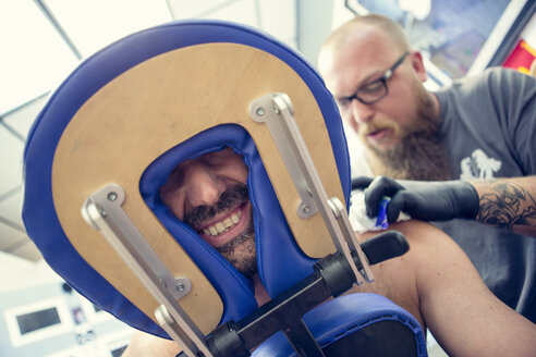 Männliche Kunden mit dem Gesicht zwischen Kopfstützen in einem Tattoo-Studio - ISF16508