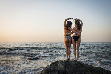 Two young women standing on rock in ocean, rear view - ISF16522