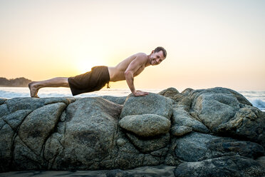 Erwachsener Mann macht Liegestütze auf Felsen am Strand - ISF16524