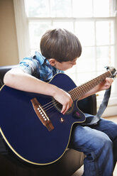 Junge spielt Gitarre auf Sofa - CUF39167