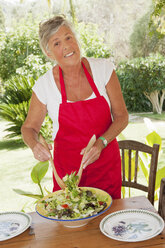Older woman tossing salad outdoors - CUF39179
