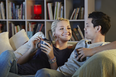 Young couple sitting on sofa with hot drinks - CUF39379