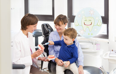 Zahnarzt lehrt Junge auf dem Schoß der Mutter das Zähneputzen - CUF39422