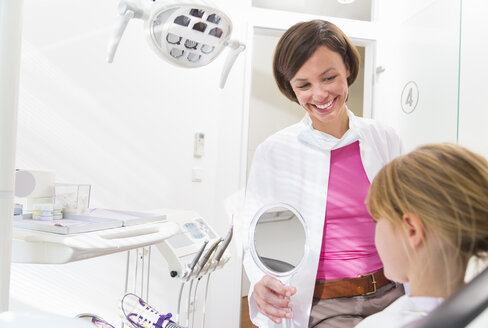 Zahnarzt hält Handspiegel vor dem Gesicht eines Mädchens - CUF39426