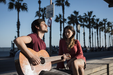 Spanien, Barcelona, Paar mit Gitarre auf einer Bank an der Strandpromenade sitzend, lizenzfreies Stockfoto