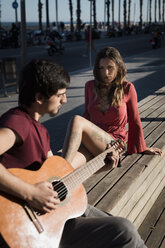 Spanien, Barcelona, Paar mit Gitarre auf einer Bank an der Strandpromenade sitzend - MAUF01445