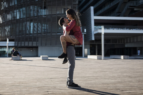 Young man lifting up happy girlfriend on city square stock photo