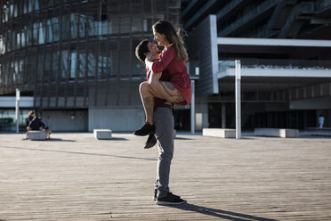 Young man lifting up happy girlfriend on city square - MAUF01454