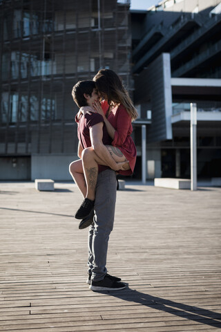 Young man lifting up girlfriend on city square stock photo