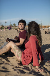 Spanien, Barcelona, lächelndes Paar mit einer Gitarre am Strand sitzend - MAUF01460