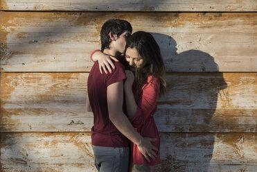 Affectionate young couple hugging and kissing at wooden wall - MAUF01475