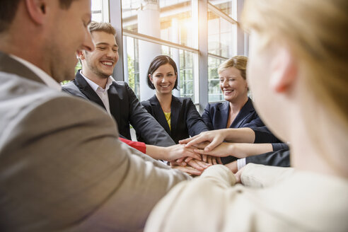 Blick über die Schulter auf eine Gruppe von Geschäftsfrauen und -männern, die sich lächelnd im Kreis die Hände reichen - ISF16579
