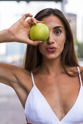 Portrait of attractive young woman wearing sports bra holding an apple - KKAF01197
