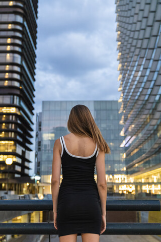 Rückansicht einer jungen Frau in einem schwarzen Kleid in der Stadt in der Abenddämmerung, lizenzfreies Stockfoto