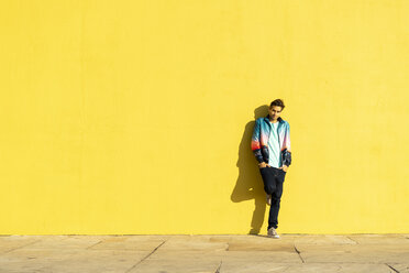 Man leaning against yellow wall with hands in pockets - AFVF00693