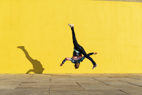 Acrobat jumping somersaults in front of yellow wall - AFVF00695