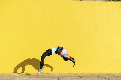 Akrobat, der vor einer gelben Wand Purzelbäume schlägt, lizenzfreies Stockfoto