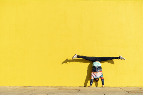 Akrobat im Handstand vor einer gelben Wand, lizenzfreies Stockfoto