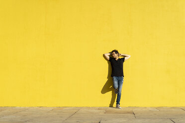 Mann lehnt mit den Händen hinter dem Kopf an einer gelben Wand - AFVF00704