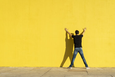 Man standing with hands on yellow wall, rear view - AFVF00705