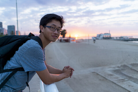Junger chinesischer Mann mit Rucksack schaut auf den Strand, lizenzfreies Stockfoto