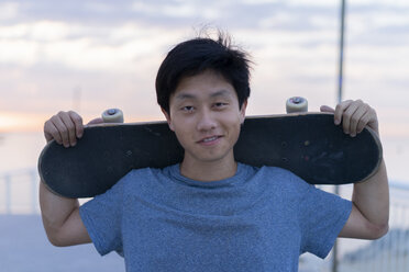 Junger chinesischer Mann mit Skateboard am Strand bei Sonnenaufgang - AFVF00714